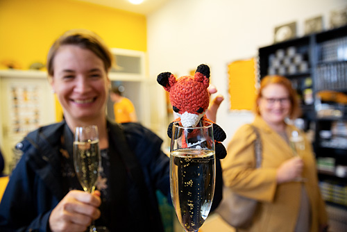 Finn der Fotofuchs wird von Fotofüchsin Tirza an ein Sektglas gehalten.